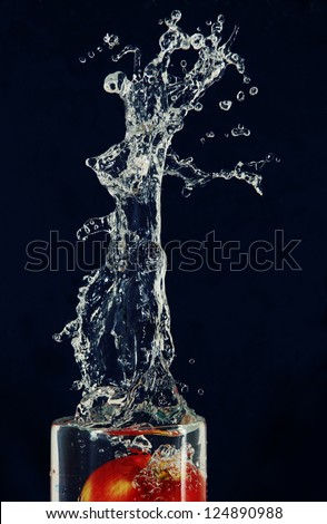 high splash and spray water from falling into a glass of apple, photo on the blue background.