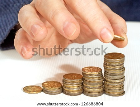 man\'s hand puts gold coins columns of different heights.