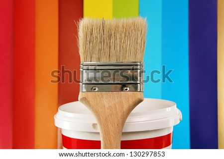 paint brush with a wooden handle and a small bucket of paint on the background of the color palette.