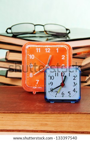 blue and orange alarm clocks, a pile of old books and glasses on the table.