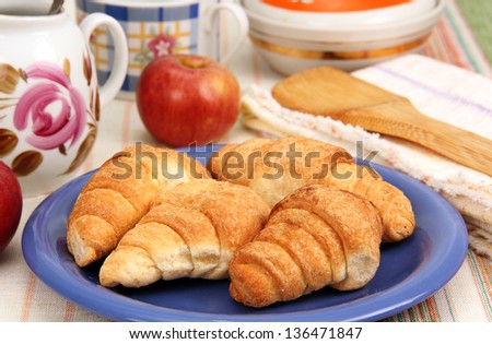 four croissant on a blue plate, apples and dishes on the dinner table.