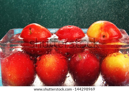 Group of ripe red plums in a glass bowl with water under a cloud of spray.