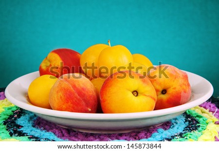 some peaches and yellow plums in a bowl on a colored napkin.