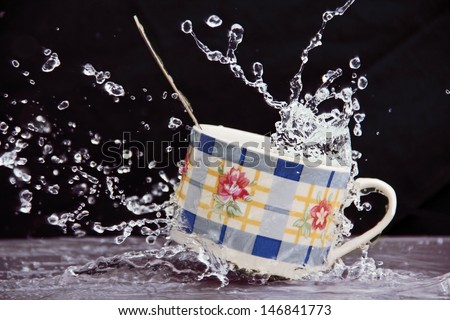 Teacup in a stream of water splashes and sprays, dark background.