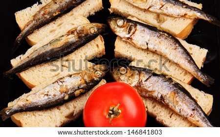 several small fried fish on slices of bread, and one whole red tomato.