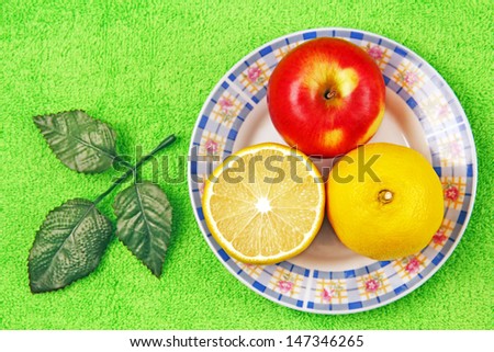 lemon, half a lemon and a whole apple lying on the plate.