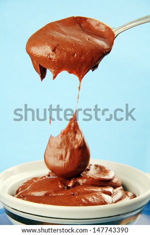 chocolate syrup dripping big drops with a metal spoon in a porcelain cup.