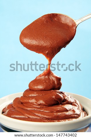 chocolate syrup dripping big drops with a metal spoon in a porcelain cup.