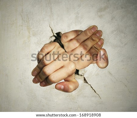 Concept of two hands trying hard to get out of breaking the wall