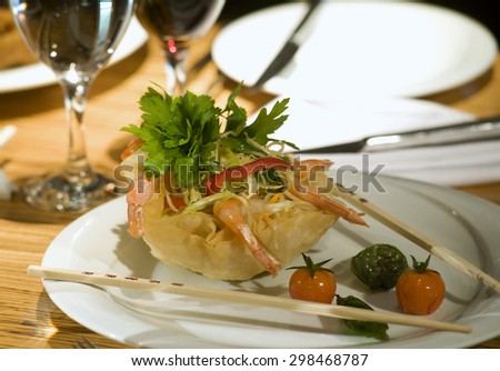 Chopsticks lift a filo pastry wrapped prawn from a plate of chinese food