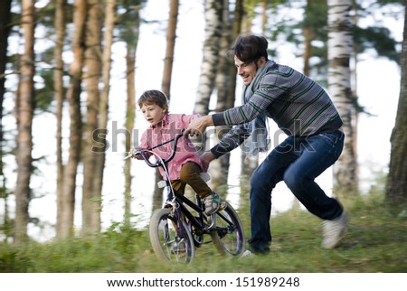 father learning his son to ride on bicycle outside