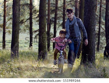 father learning his son to ride on bicycle outside