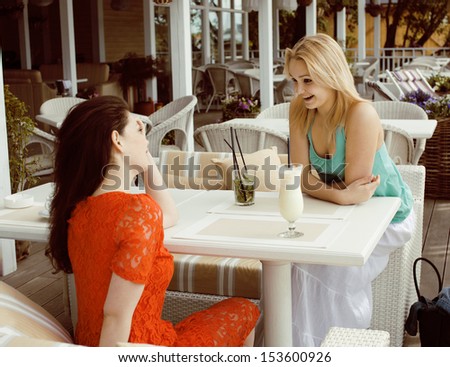 portrait of two pretty friends in cafe drinking and talking