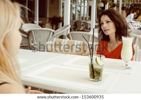 portrait of two pretty friends in cafe drinking and talking