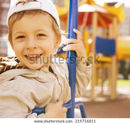 little cute boy on swing outside, playground background, smiling close up
