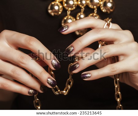 close up photo hands with gold manicure holding chain on black