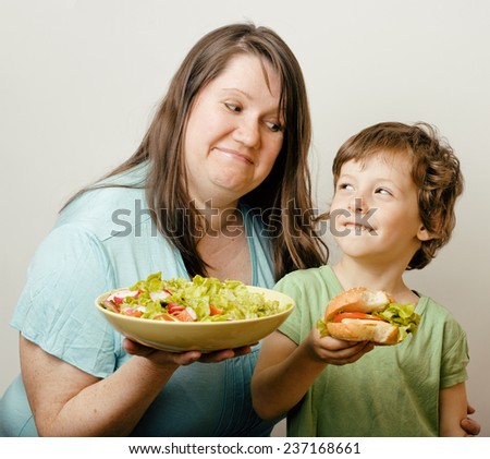 fat woman holding salad and little cute boy with hamburger teasing, real family scene.