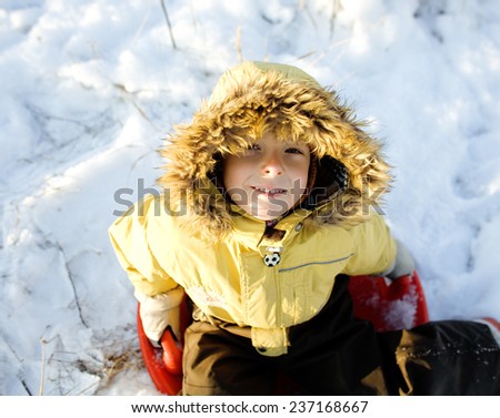 little cute boy in hood with fur on snow outside smiling