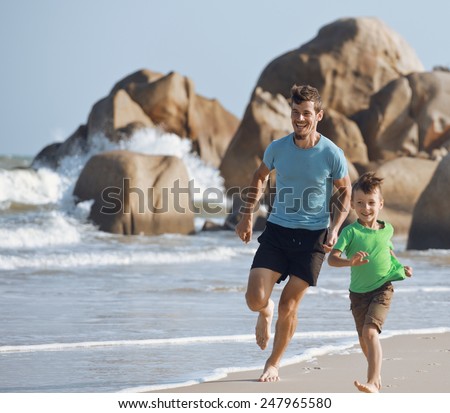 happy family on beach playing, father with son walking sea coast, rocks behind