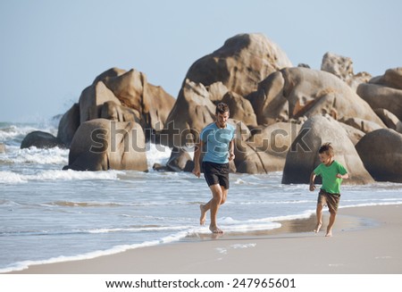 happy family on beach playing, father with son walking sea coast, rocks behind