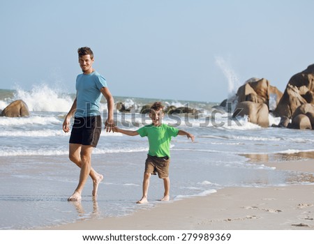 happy family on beach playing, father with son walking sea coast, rocks behind smiling enjoy summer warm