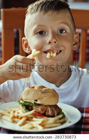 little cute boy 6 years old with hamburger and french fries making crazy faces in restaurant close up