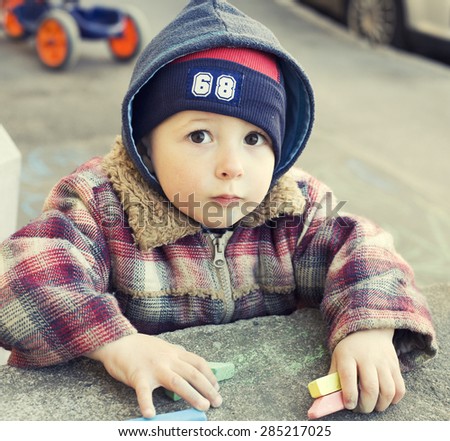 portrait of little cute boy writing with chalk on the ground, preschooler