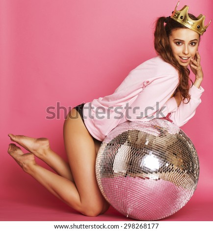 young cute party girl on pink background with disco ball and crown smiling