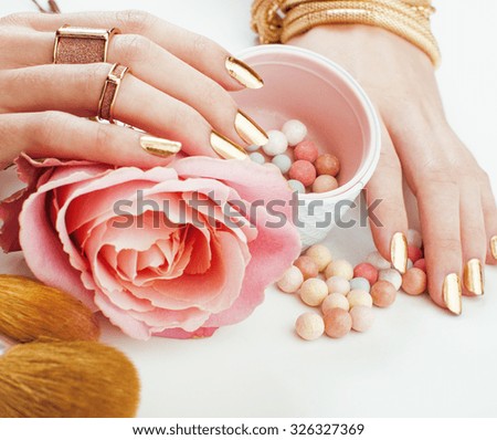 woman hands with golden manicure and many rings holding brushes, makeup artist stuff stylish, pure close up, pink tender rose flower