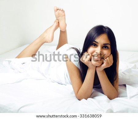 pretty indian brunette real woman in bed smiling, white sheets, tan skin close up thinking