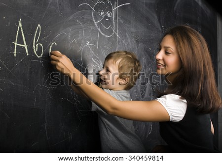 little cute boy with young teacher in classroom studying at blackboard smiling