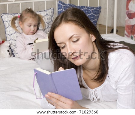 portrait of mother and daughter laying in bed reading and writing