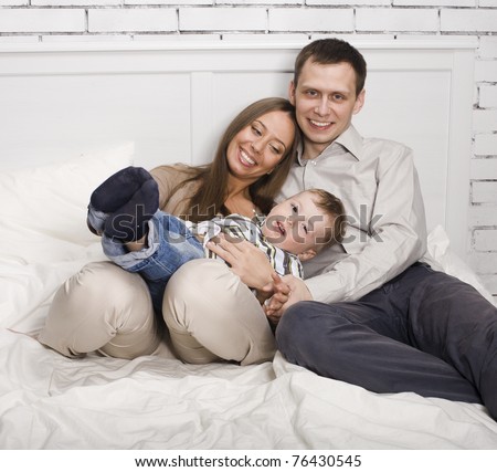 portrait of happy family, mom and dad playing with their son in bed