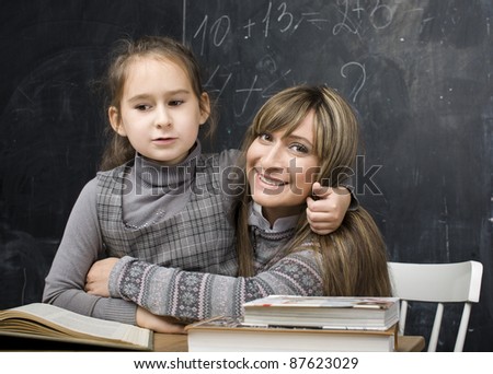 portrait of little girl with mother hugging at blackboard, making lessons