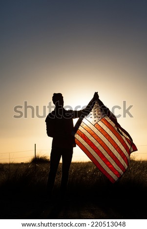 Young man proudly waving the American flag at sunset