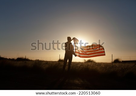 Young man proudly waving the American flag at sunset