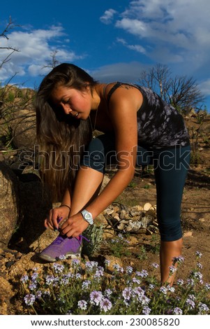 Young woman stops to tie her shoes during a beautiful hike