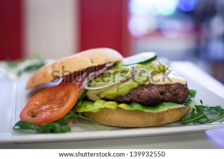 An open hamburger sandwich on a plate showing the patty meat, the tomato, lettuce, mayo and onion
