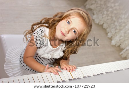 beautiful blond little girl with blue eyes in pretties sitting near a piano and  looking at camera