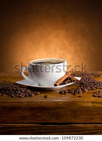 coffee cup, coffee beans and cinnamon sticks on dark background