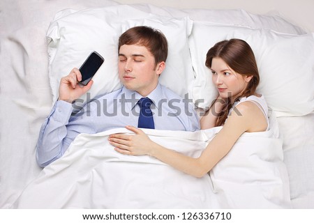 man obsessed by work in bed with beautiful woman
