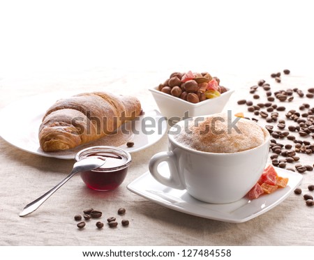 breakfast in cafe - cappuccino, croissant, nut, jam and candied fruits on tableware on white background