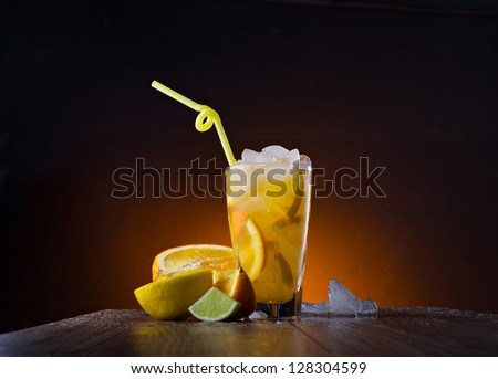 On a wooden table with water drop standing misting glass with mix cocktail, and near lying slice  of lime, lemon and orange on dark-brown background