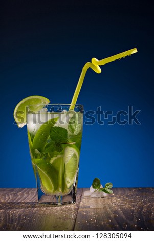 fresh drink with citrus fruit, ice and mint standing on a wooden table on blue background