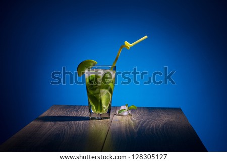 alcoholic beverage with tropical fruit, ice and mint on wooden table on blue background
