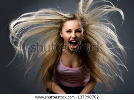 portrait of screaming young woman with long blond flying hair on dark-grey background