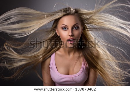 portrait of a amazed blond young woman with waving hair and opened mouth on grey-dark background
