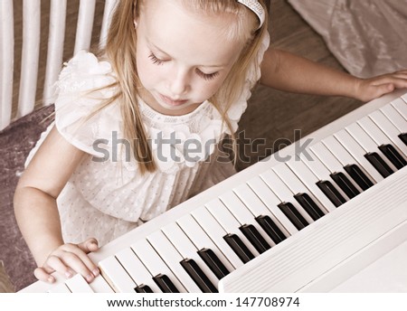 little beauty well-dressed girl  playing on white piano, top view
