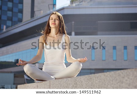 young woman sitting with crossed legs in yoga pose on modern building background