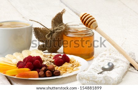 coffee, honey and beautiful dessert with fruits slices, raspberry, nuts and flakes on wooden plank table